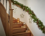 Kerstelijk versierde houten trap met verlichte dennenguirlande, groene kerstballen, rode bessen, lantaarns en kaarsen, vanuit een laag frontaal perspectief naar boven gefotografeerd