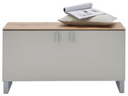 Garderobenbank mit Holzoberfläche, zwei Türen und silbernen Griffen, frontal fotografiert. Auf der Bank liegt ein Kissen und eine aufgeschlagene Zeitschrift.