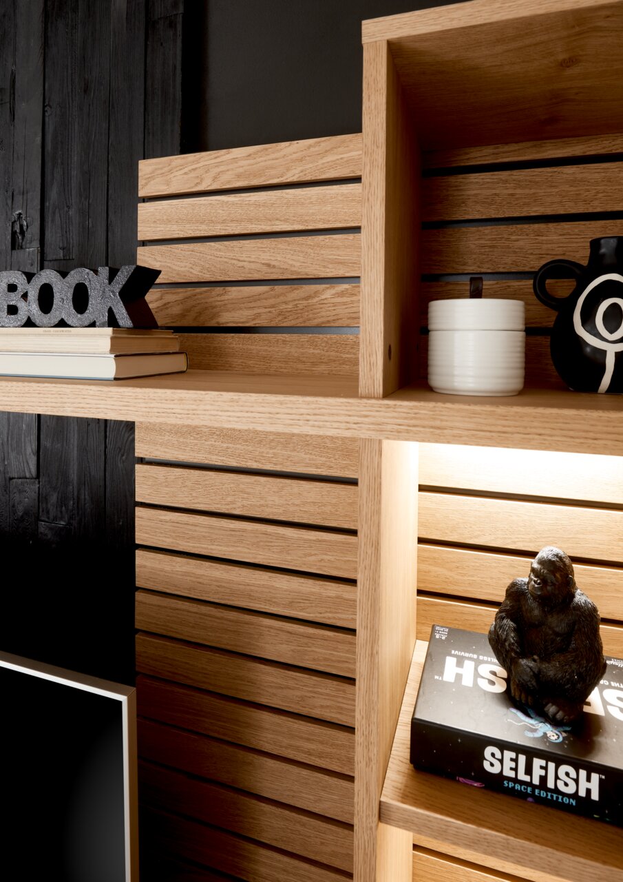 Nahaufnahme eines modernen Holzregals mit dekorativen Gegenständen, darunter Bücher, eine schwarze Vase und eine Gorilla-Figur. Perspektive von schräg oben.