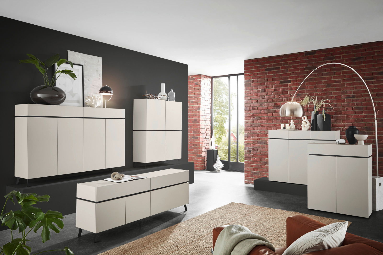 Voleo Brede ladekast UNIQUE Moderne Wohnzimmermöbel in einem stilvollen Raum mit Backsteinwand, bestehend aus Kommoden und Sideboards in cremefarbenem Design, seitliche Perspektive.