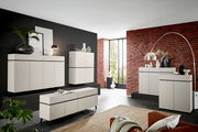 Moderne Wohnzimmermöbel in einem stilvollen Raum mit Backsteinwand, bestehend aus Kommoden und Sideboards in cremefarbenem Design, seitliche Perspektive.