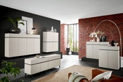 Moderne woonkamermeubels in een stijlvolle ruimte met een bakstenen muur, bestaande uit ladekasten en dressoirs in een crèmekleurig ontwerp, zijaanzicht.