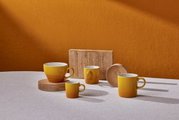Vier gelbe Becher in verschiedenen Größen auf einem Tisch, mit einem warmen orangefarbenen Hintergrund, aus seitlicher Perspektive fotografiert.