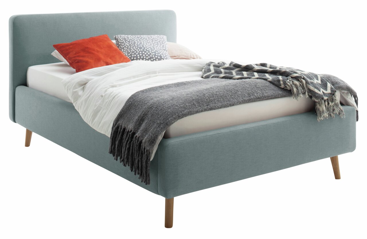 Z2 Polsterbett MATTIS Polsterbett in hellblauem Stoff mit Holzfüßen, dekoriert mit Kissen und Decken, seitliche Perspektive