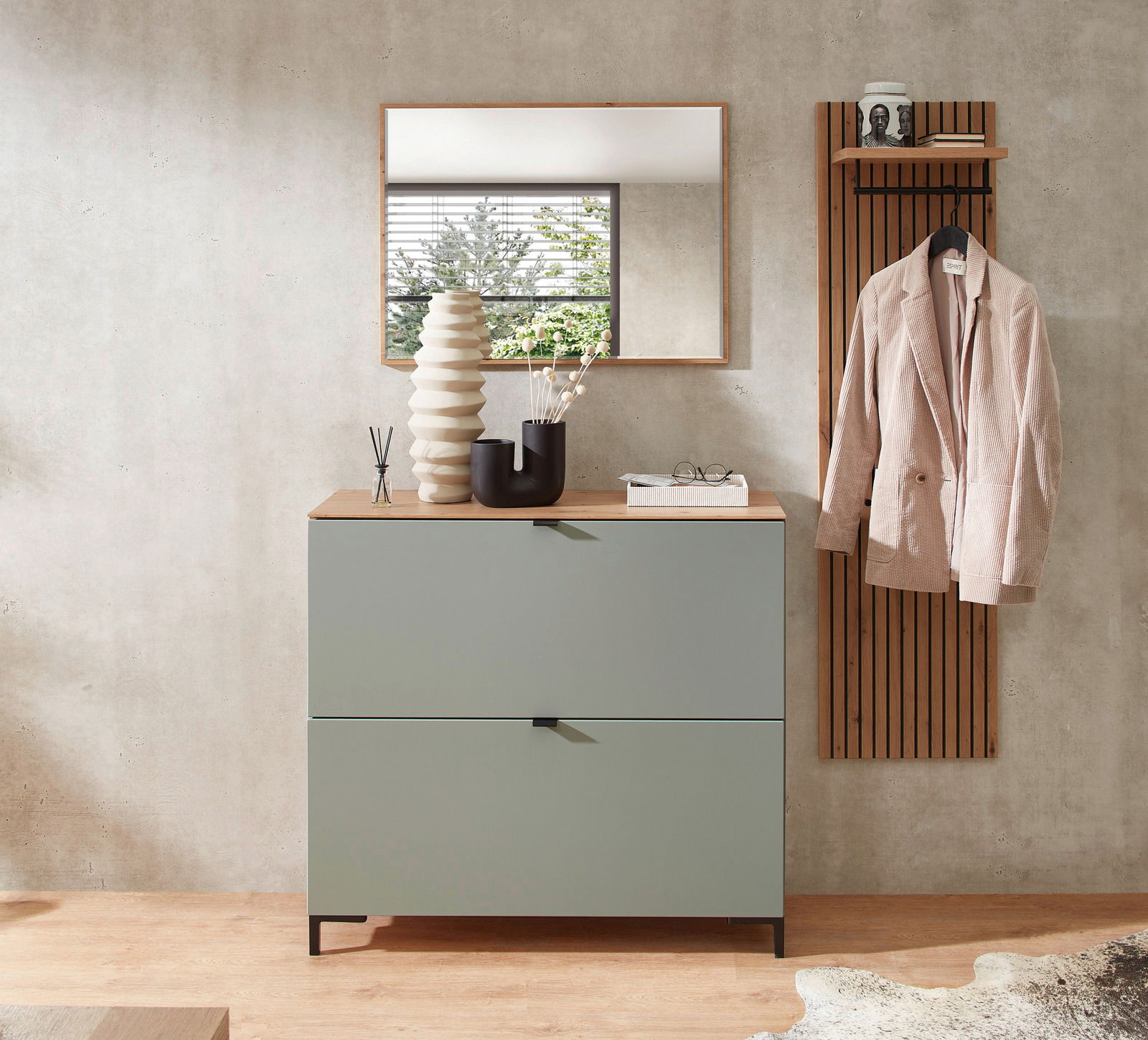 Moderner Garderobenbereich mit einem grünen Hänge-Schuhschrank, einem Spiegel und einer Garderobenleiste mit Jacke, aus der Frontalperspektive fotografiert.