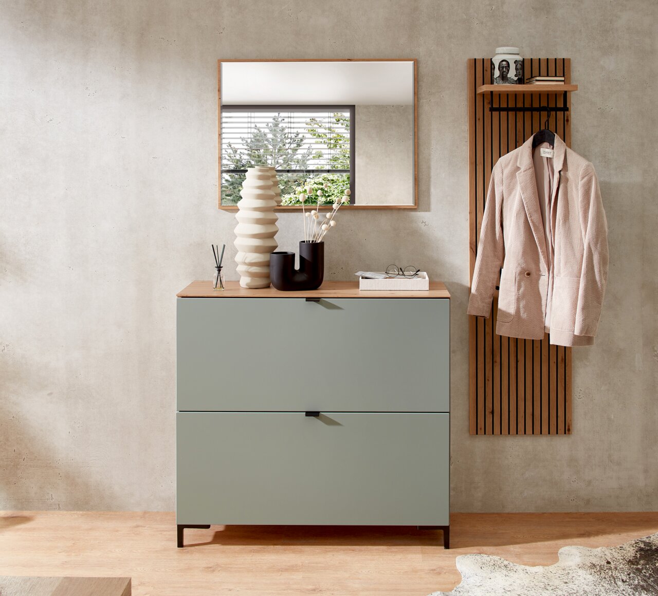 Moderne garderobe met een groene hangende schoenenkast, een spiegel en een kapstok met een jas, gefotografeerd vanuit een vooraanzicht.