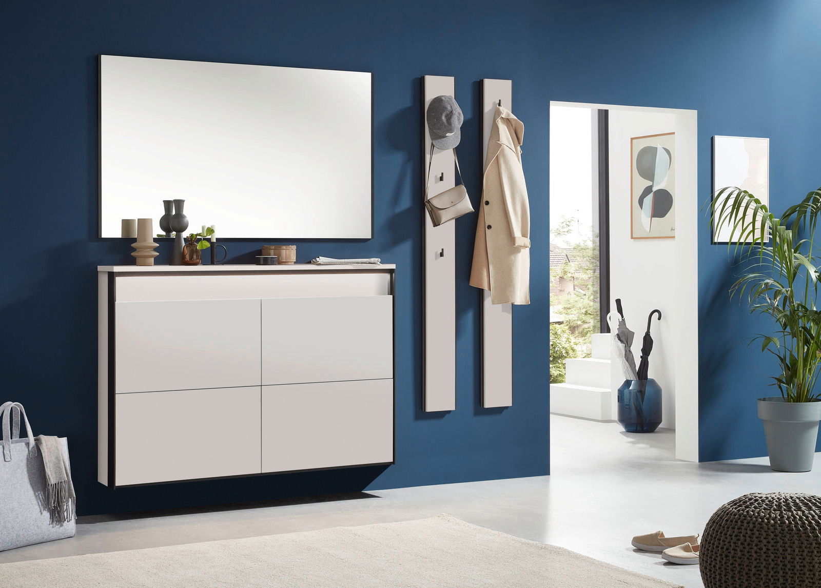 Voleo Garderobenpaneel-Set ZAYA Moderner Eingangsbereich mit weißem Hängeschuhschrank und Garderobenpaneelen an einer blauen Wand, seitliche Perspektive.