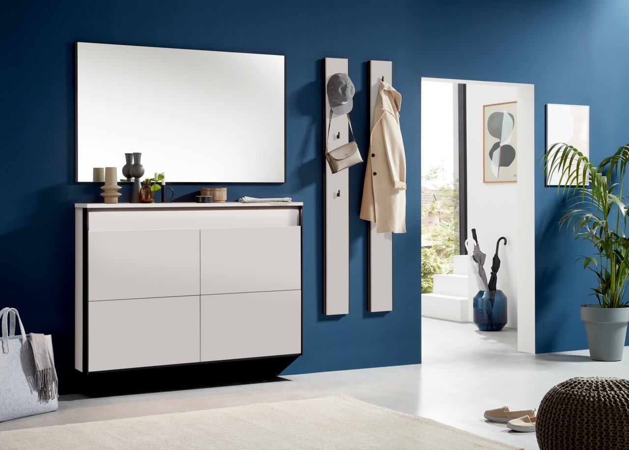 Moderner Eingangsbereich mit weißem Hängeschuhschrank und Garderobenpaneelen an einer blauen Wand, seitliche Perspektive.