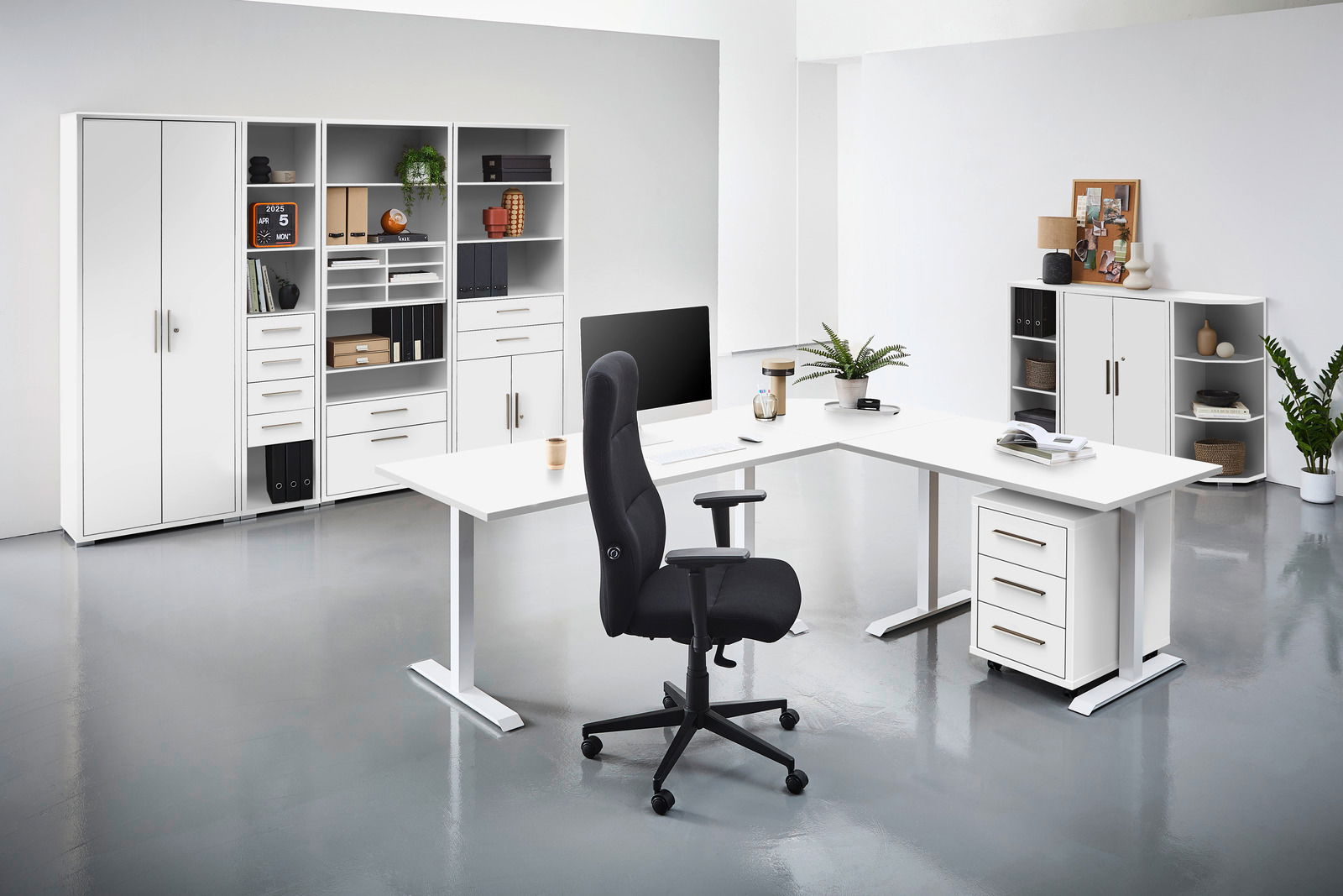 Moderne Büroumgebung mit weißen Schreibtischen, Regalen und einem schwarzen Bürostuhl, aus der Perspektive von vorne betrachtet.