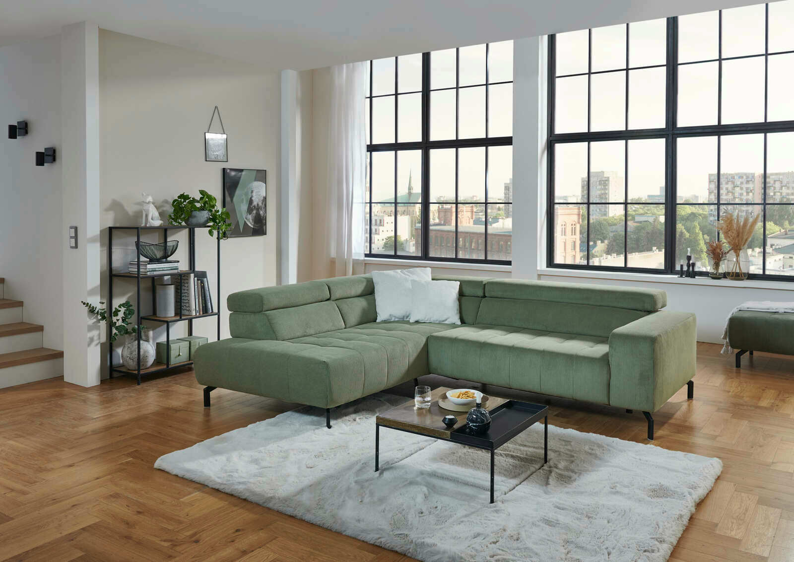 Grüne Eckgarnitur in modernem Wohnzimmer mit großen Fenstern, Holzboden und stilvollem Dekor, seitliche Perspektive.