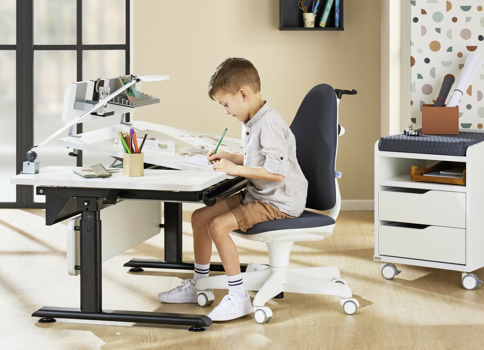 Ein Kind sitzt auf einem modernen Jugenddrehstuhl an einem höhenverstellbaren Schreibtisch, seitliche Perspektive.