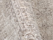 Nahaufnahme eines Designer Teppichs mit antikem Muster in Beige- und Grautönen, perspektivisch von der Seite aufgenommen.