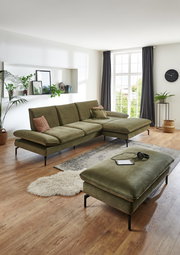Rechteckiger Hocker in einem modernen Wohnzimmer, aus olivgrünem Stoff mit schwarzen Metallbeinen, im Vordergrund der Perspektive.