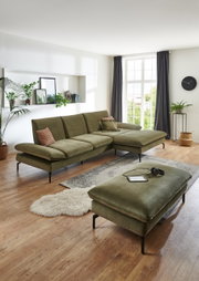 Rechteckiger Hocker in einem modernen Wohnzimmer, aus olivgrünem Stoff mit schwarzen Metallbeinen, im Vordergrund der Perspektive.