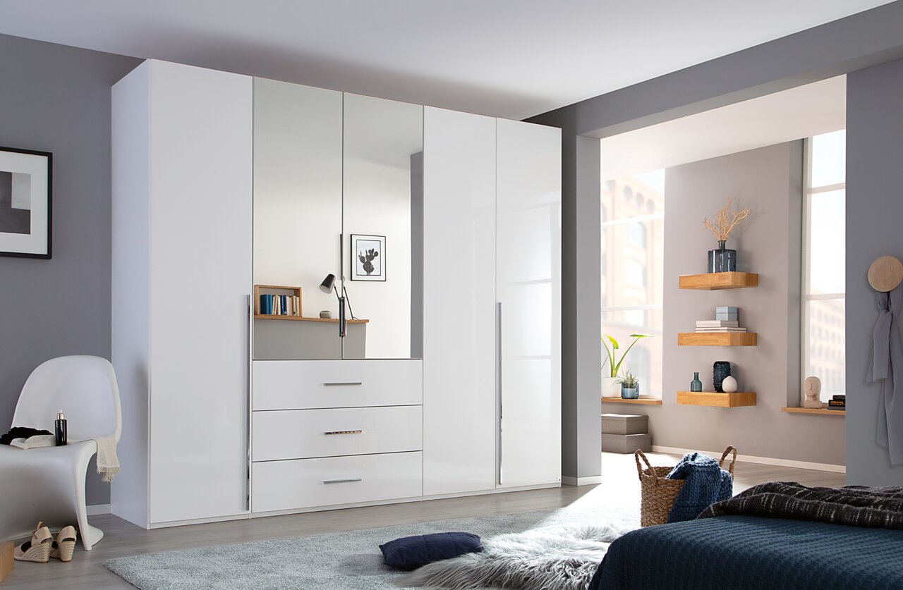 Moderne witte kast met draaideuren en spiegel in een stijlvol ingerichte slaapkamer, gezien vanaf de zijkant.