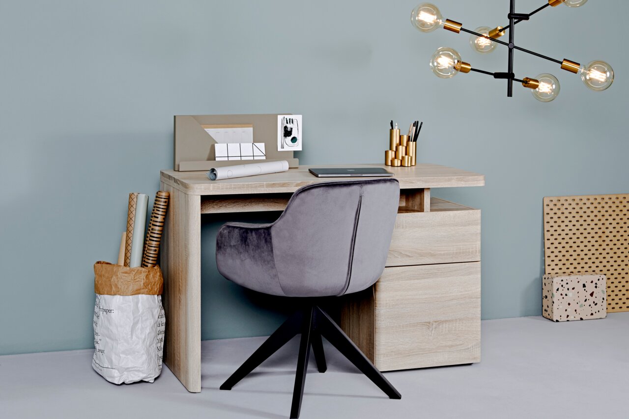 Moderner Schreibtisch in Holzoptik mit Schubladen, grauer Drehstuhl und stilvolle Dekorationen, seitliche Perspektive.