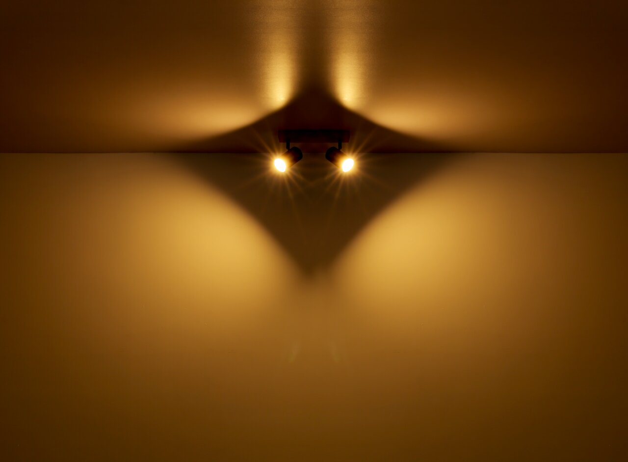 Zwei Strahler aus Metall in Graphit dunkel, an der Decke montiert, werfen warmes Licht und erzeugen ein interessantes Schattenspiel. Perspektive von unten.