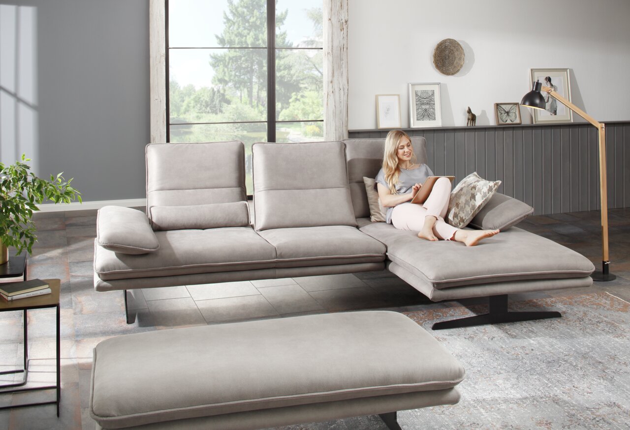 Moderne Longchairkombination in einem hellen Wohnzimmer mit einer Frau, die entspannt auf dem Sofa sitzt. Perspektive von vorne.