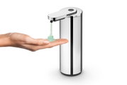 Automatischer Seifenspender aus Edelstahl in Silber mit Sensor und Auslauf, der grünes Gel in eine ausgestreckte Hand dosiert, freigestellt auf weißem Hintergrund, Perspektive: frontale leicht schräge Seitenansicht.