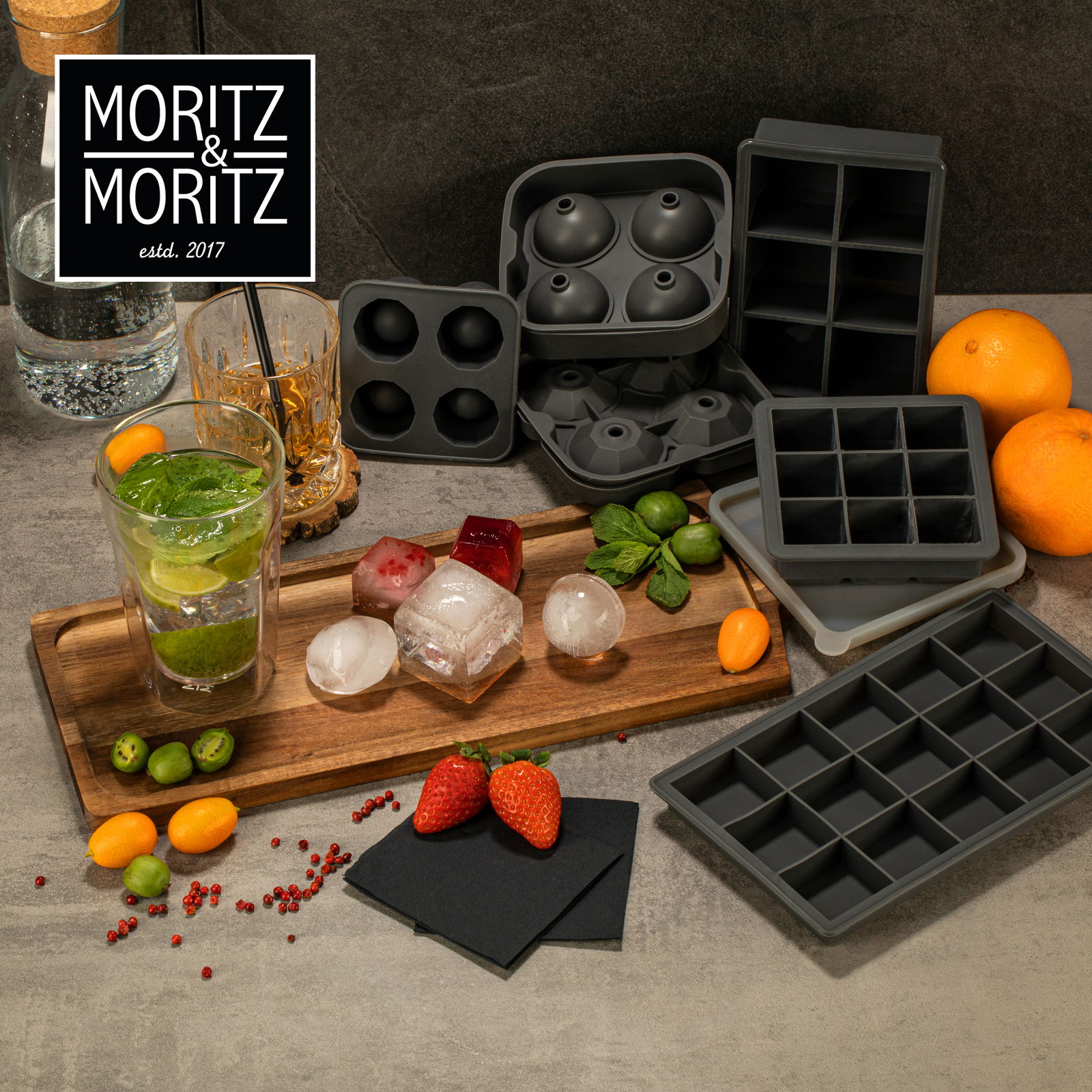 Verschiedene Eiswürfelformen aus Silikon in verschiedenen Formen, darunter Kugeln und Würfel, auf einer Küchenarbeitsplatte mit frischen Früchten und Getränken, aus der Vogelperspektive.