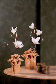 Zwei dekorative Vasen mit weißen Blumen auf einem Holztisch, fotografiert aus einer seitlichen Perspektive.