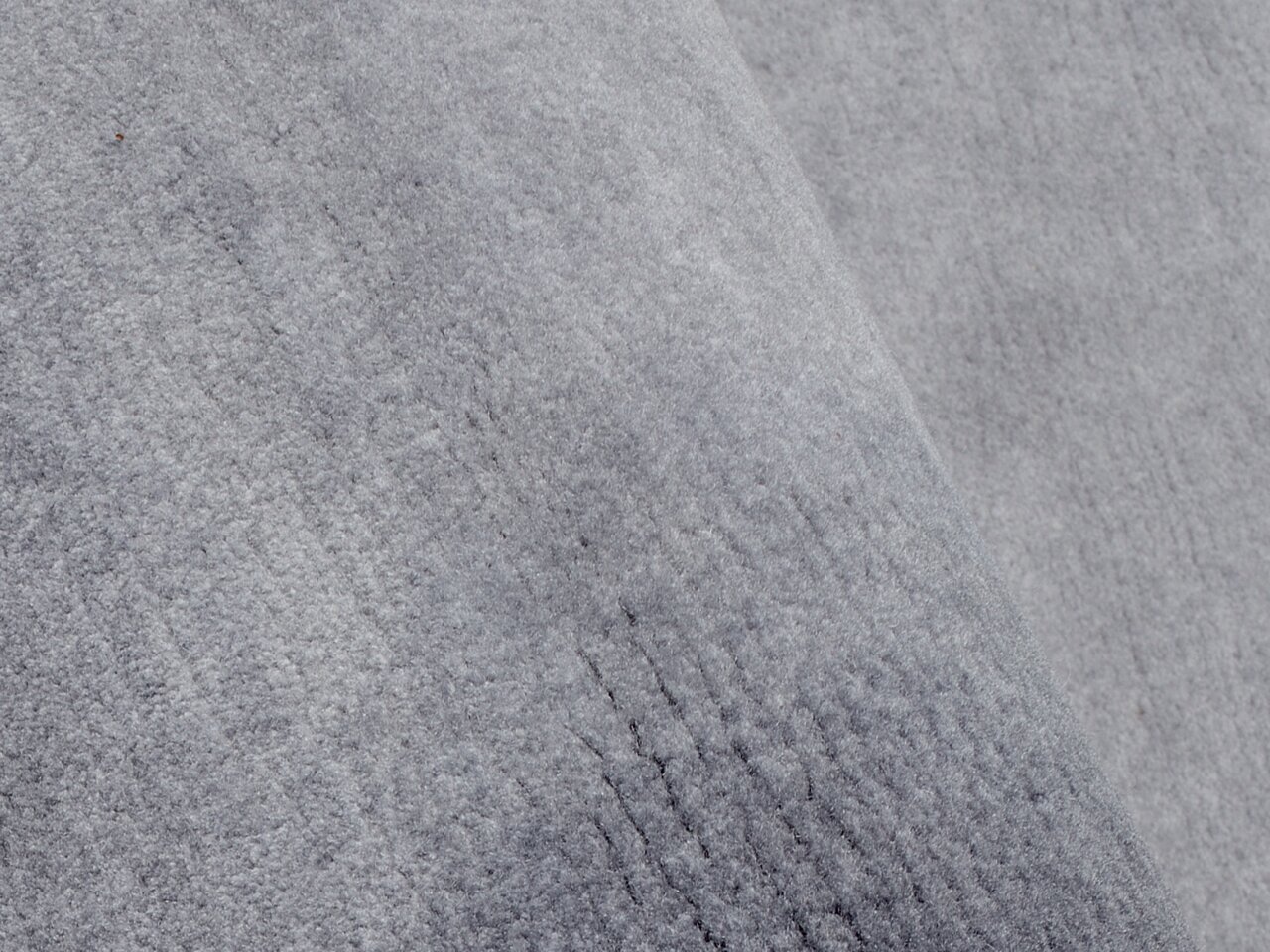 Nahaufnahme eines grauen Wollteppichs mit weicher Textur, schräg von oben fotografiert.