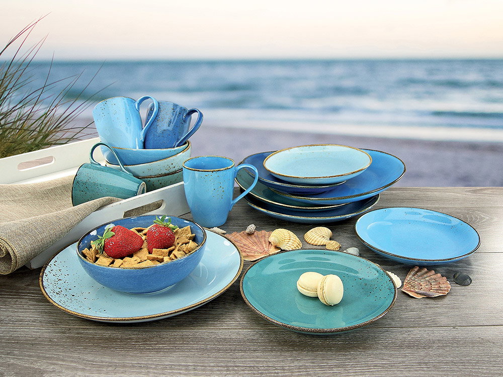 Blauw servies op een tafel met een strand op de achtergrond.