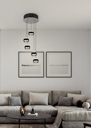 Moderne Pendelleuchte Orbit mit fünf kugelförmigen Lampen, hängend von einer schwarzen Deckenhalterung, in einem stilvollen Wohnzimmer mit grauem Sofa und minimalistischer Dekoration. Perspektive von vorne.