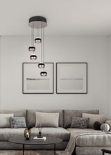 Moderne Pendelleuchte Orbit mit fünf kugelförmigen Lampen, hängend von einer schwarzen Deckenhalterung, in einem stilvollen Wohnzimmer mit grauem Sofa und minimalistischer Dekoration. Perspektive von vorne.