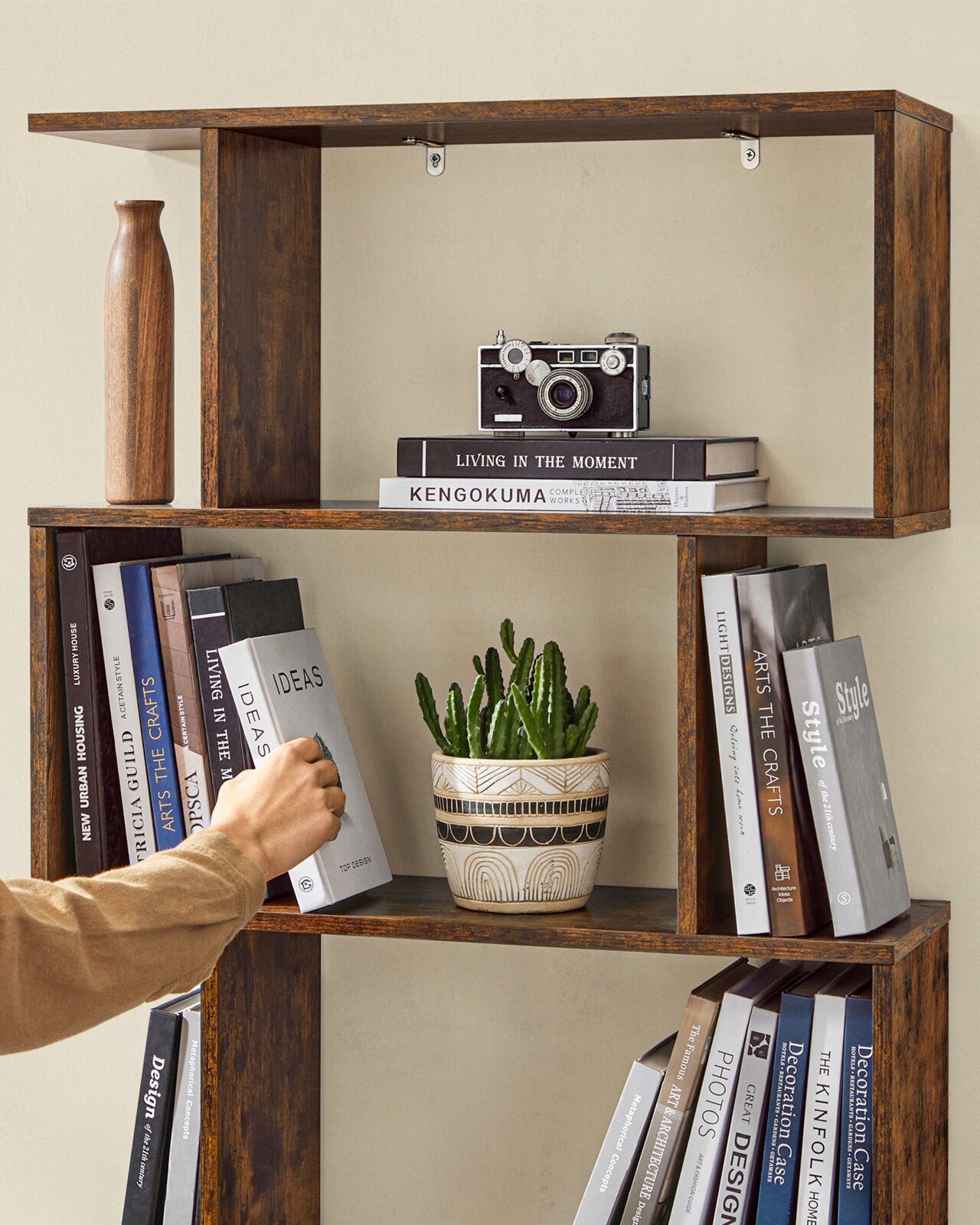 Modernes, dunkelbraunes Holz-Wandregal mit offenen Fächern, dekoriert mit Büchern, Vintage-Kamera, Vase und Topfpflanze; Frontansicht leicht von links.