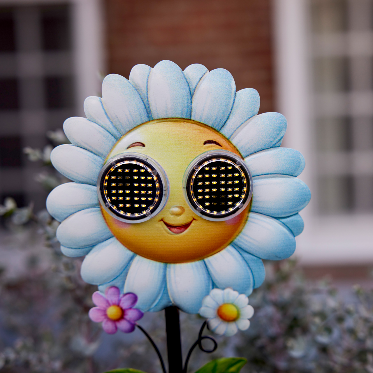 Frontalansicht einer Solar Stabbeleuchtung in Form einer lächelnden Blume mit blauen Blütenblättern und LED-Augen.
