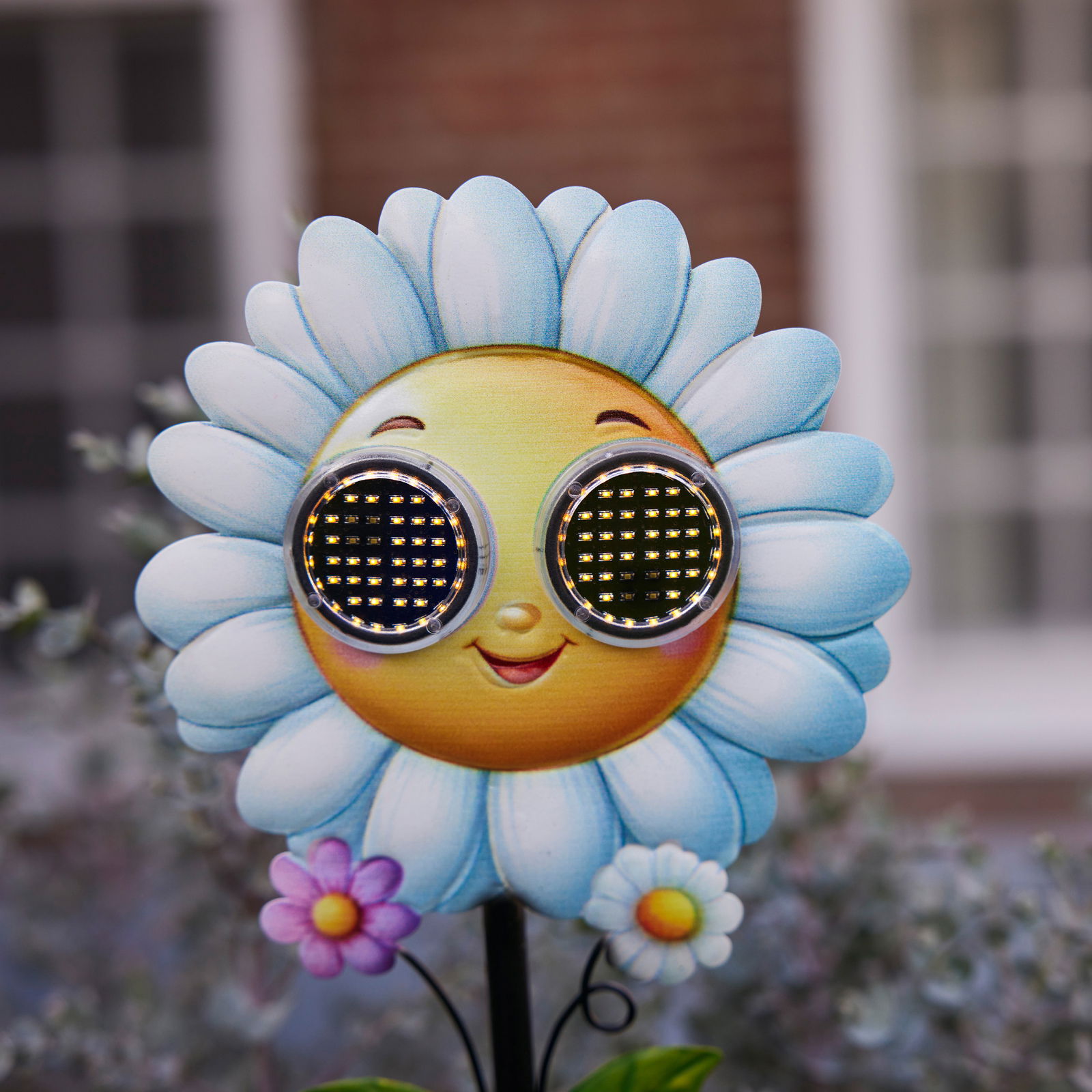 Frontalansicht einer Solar Stabbeleuchtung in Form einer lächelnden Blume mit blauen Blütenblättern und LED-Augen.