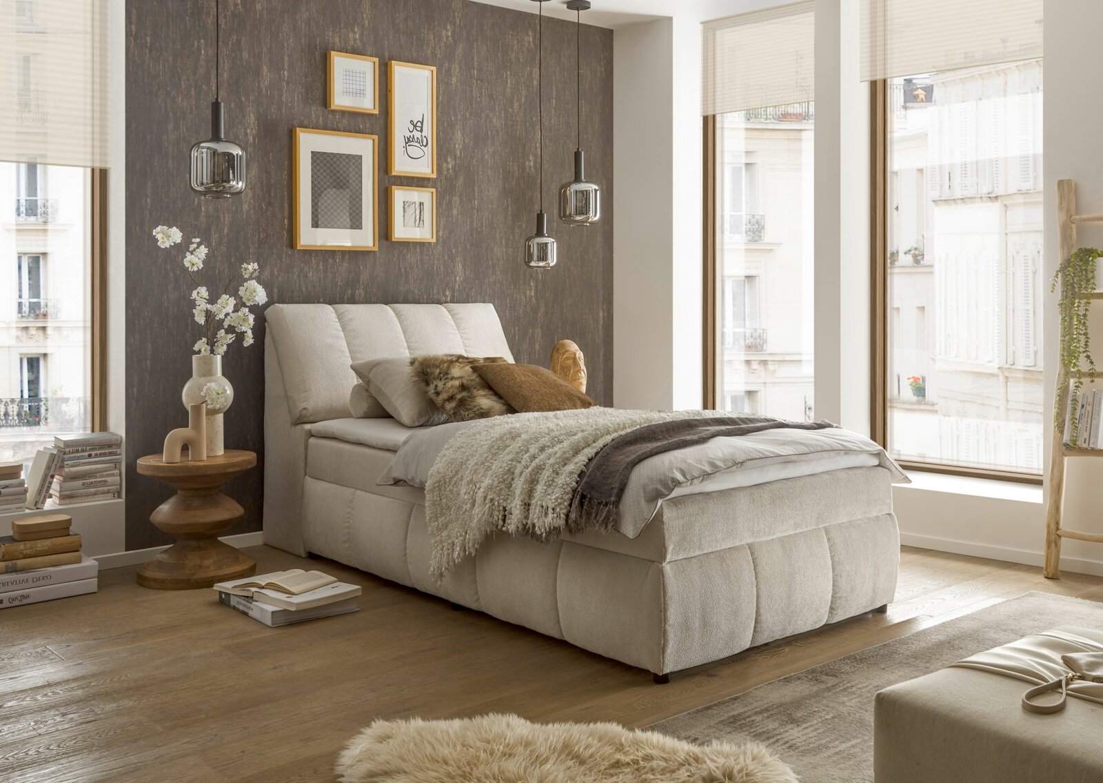 Gemütliches Boxspringbett in einem modernen Schlafzimmer mit großen Fenstern, seitliche Perspektive.