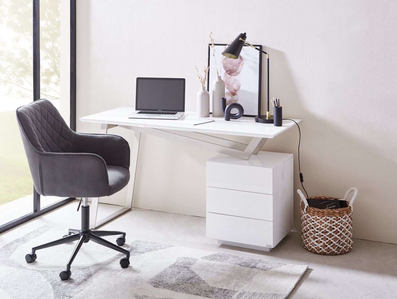 Moderner Schreibtisch mit weißer Oberfläche, seitlicher Perspektive, ausgestattet mit Laptop, Lampe und Dekorationen, neben einem grauen Bürostuhl.