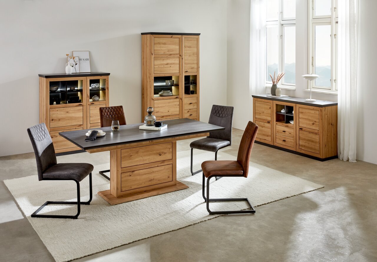 Hom´in Functionele eettafel BENTON Moderner Funktions-Esstisch aus Holz mit dunkler Tischplatte, umgeben von vier Stühlen in einem hellen Raum mit großen Fenstern, aus der Perspektive von vorne.