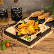 Servierset aus Bambus mit fünf schwarzen Schalen, gefüllt mit Dips und Nachos, auf einem Holztisch von oben fotografiert.