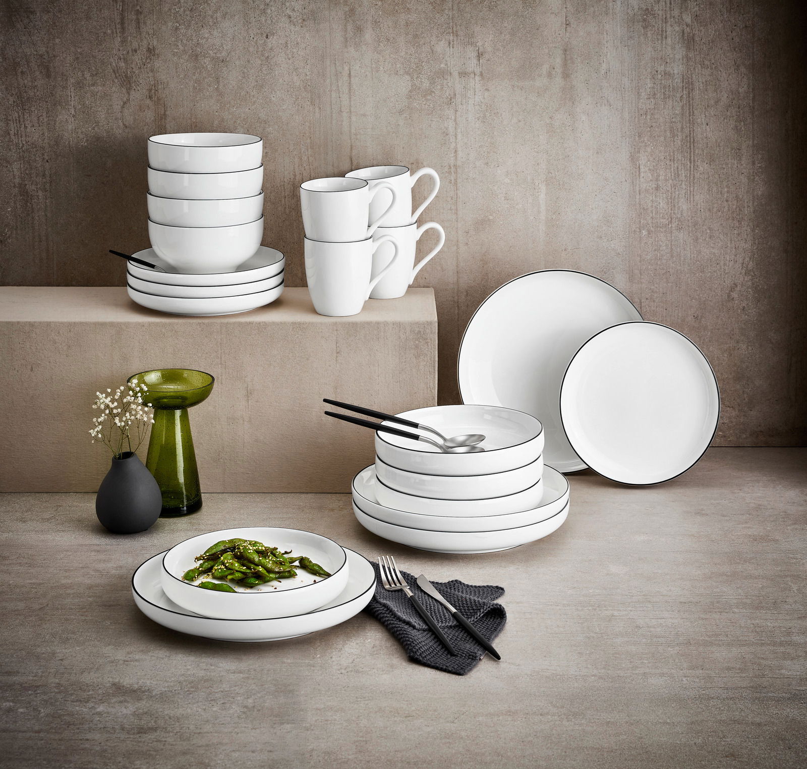 Elegantes weißes Kombiservice 20-tlg. mit schwarzem Rand, bestehend aus Tellern, Schalen und Tassen, stilvoll arrangiert auf einem Tisch mit moderner Dekoration. Seitliche Perspektive.