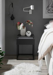 Moderne Nachtkommode in dunklem Design mit geriffelter Front, dekoriert mit einer Vase und einer Uhr, seitliche Perspektive.