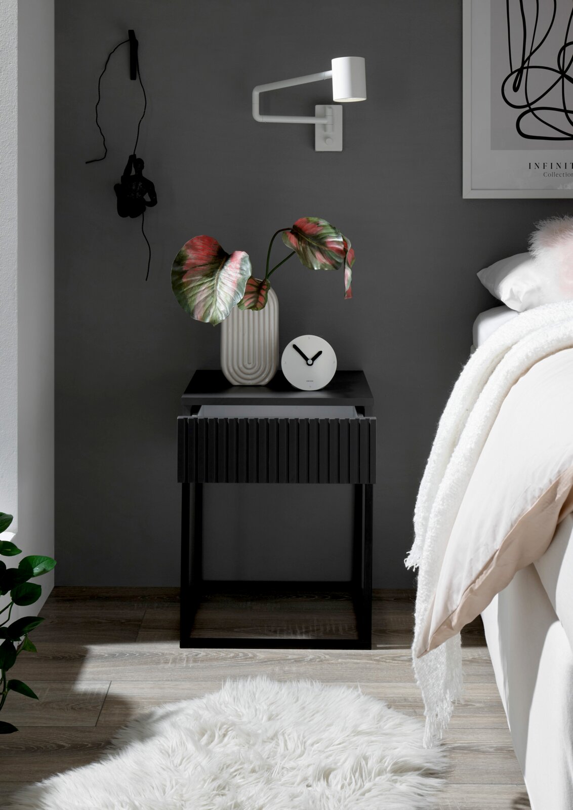 Moderne Nachtkommode in dunklem Design mit geriffelter Front, dekoriert mit einer Vase und einer Uhr, seitliche Perspektive.