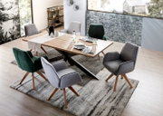 Moderne eettafel met houten blad en X-vormig metalen onderstel, omringd door gestoffeerde stoelen in grijs en groen, gefotografeerd vanuit vogelperspectief.