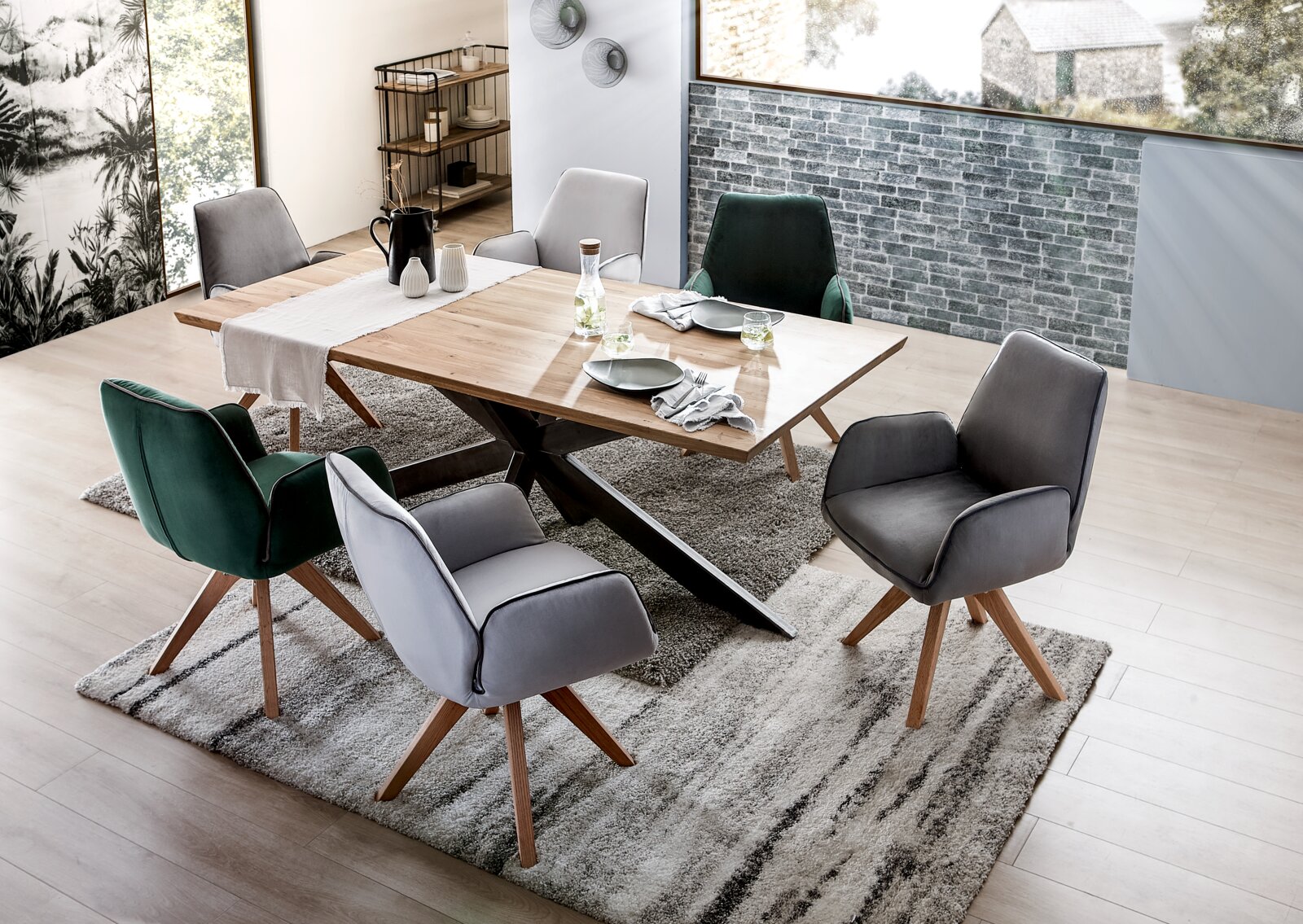 Moderne eettafel met houten blad en X-vormig metalen onderstel, omringd door gestoffeerde stoelen in grijs en groen, gefotografeerd vanuit vogelperspectief.