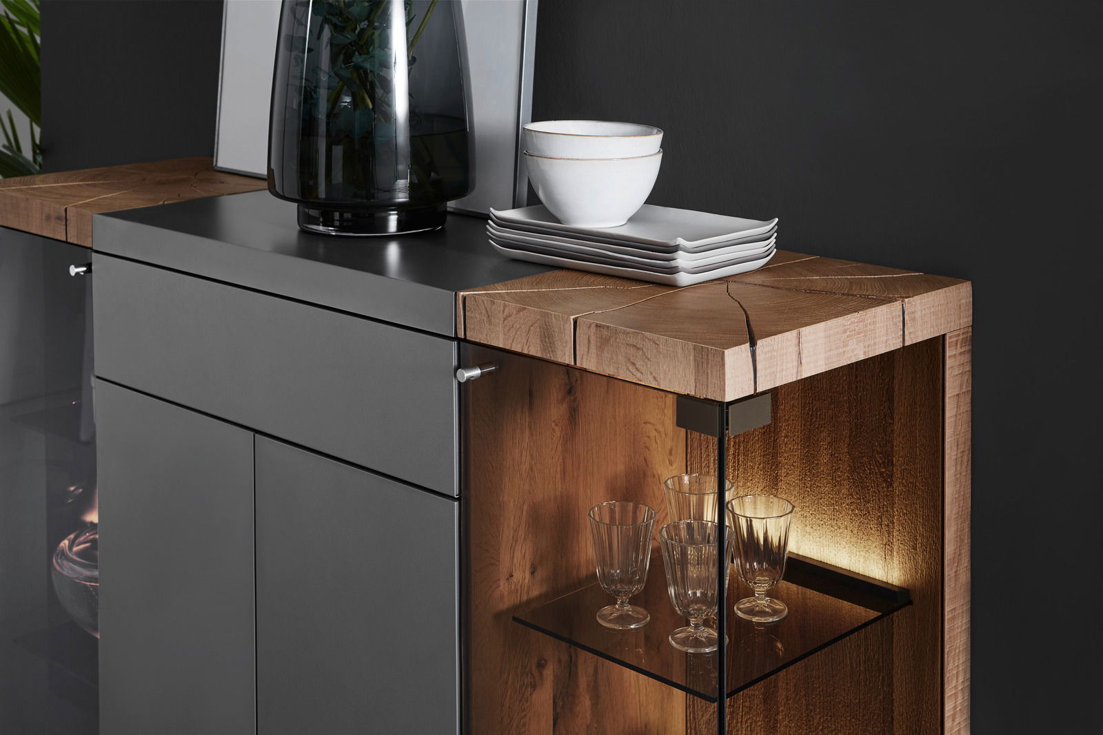 Detailansicht eines modernen Highboards mit dunkler Front und Holzdetails, dekoriert mit Geschirr und Gläsern.