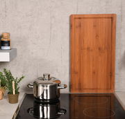 Rechteckige Schneide- und Abdeckplatte aus Holz, stehend auf einer Küchenarbeitsplatte neben einem Topf und Gewürzglas, aus frontaler Perspektive.