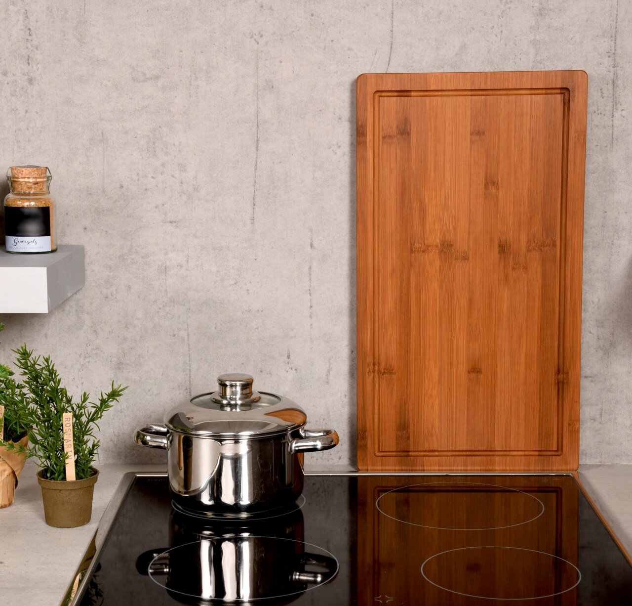 Rechteckige Schneide- und Abdeckplatte aus Holz, stehend auf einer Küchenarbeitsplatte neben einem Topf und Gewürzglas, aus frontaler Perspektive.