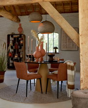 Moderner Esstisch mit runder Tischplatte und konischem Sockel, umgeben von vier gepolsterten Stühlen in einem gemütlichen Raum mit rustikalen Holzbalken, aus der Frontalperspektive.