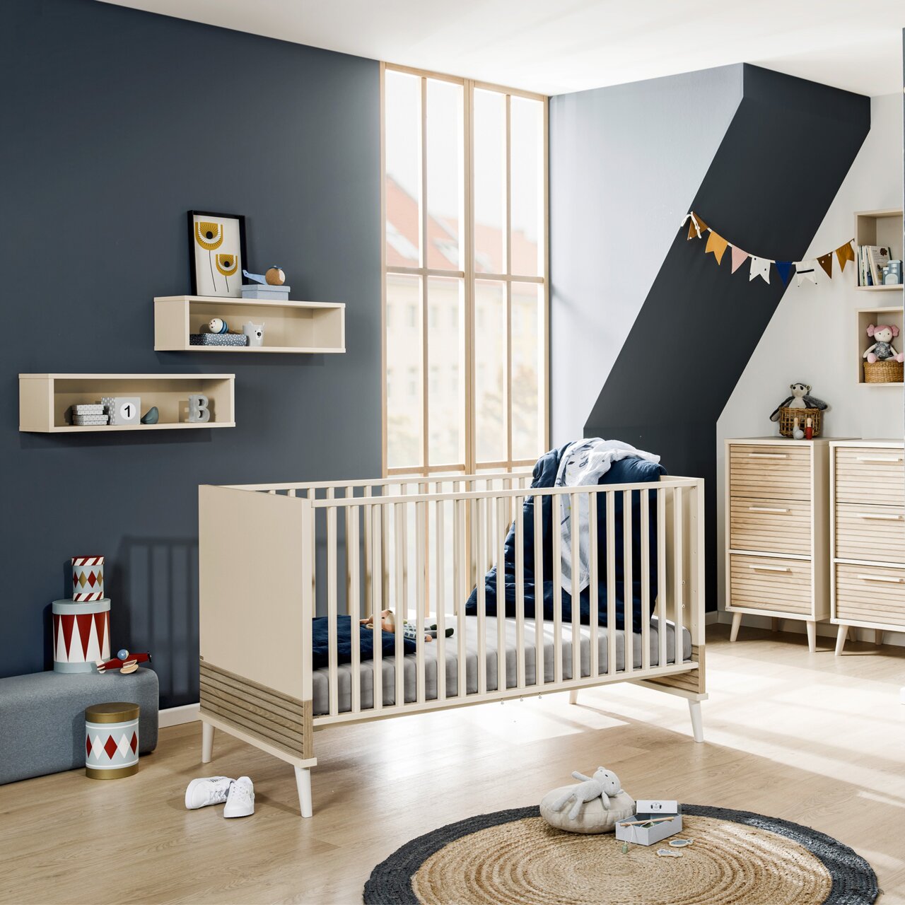 Een modern babybedje in een stijlvol ingerichte kinderkamer, gezien vanaf de zijkant van het bed.
