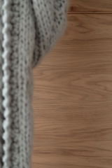 Nahaufnahme einer Holzoberfläche mit einem gestrickten Stoff im Vordergrund, seitliche Perspektive.
