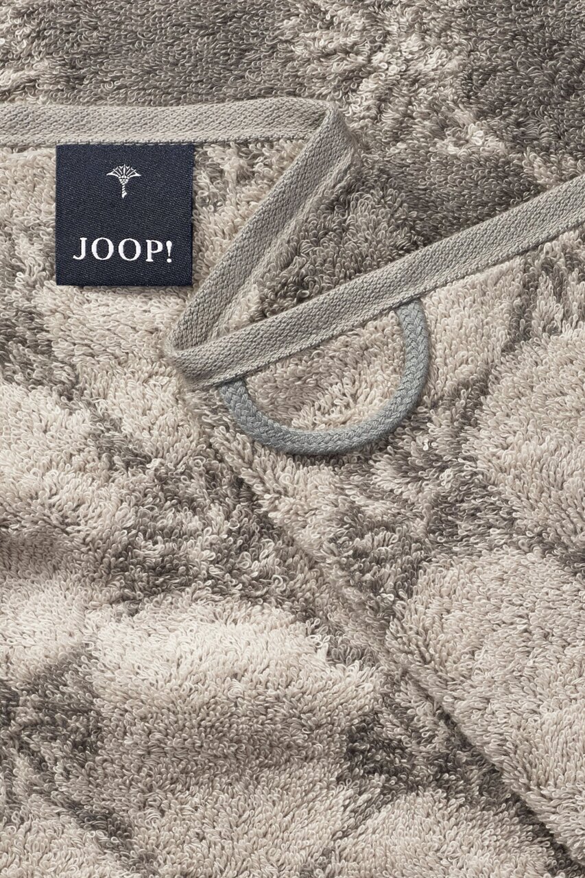 Close-up van een handdoek met patroon in grijze en beige tinten, met het merklabel 'JOOP!' duidelijk zichtbaar.