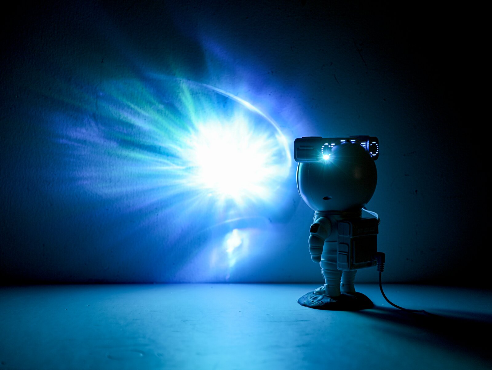 LED-Dekoleuchte in Form eines Astronauten, der eine leuchtende Projektion an die Wand wirft, seitliche Perspektive.