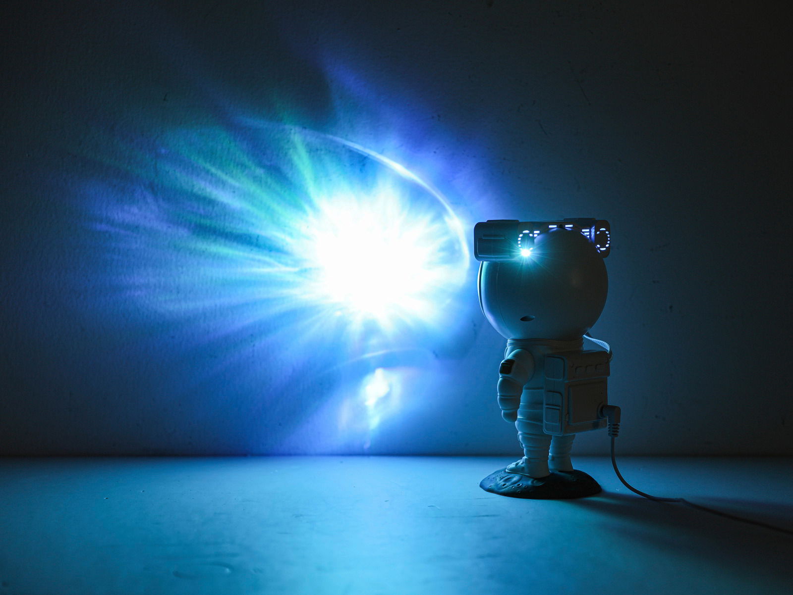 LED-Dekoleuchte in Form eines Astronauten, der eine leuchtende Projektion an die Wand wirft, seitliche Perspektive.